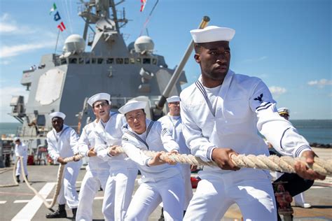 A group of sailors shouting Hoo-Rah, with a naval ship in the background