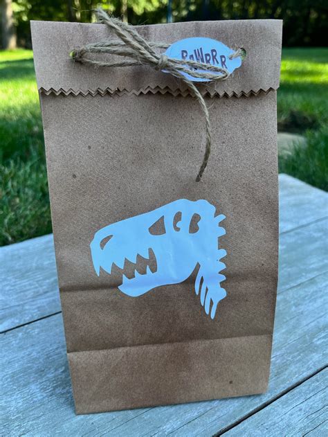 A paper bag featuring a dinosaur design and handles made from yarn