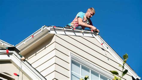 A handyman hanging Christmas lights on a roof