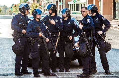 Image of a police officer in riot gear holding a military-style rifle