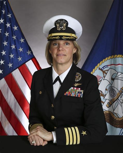 A Navy officer in uniform, with a Navy logo and American flag in the background.