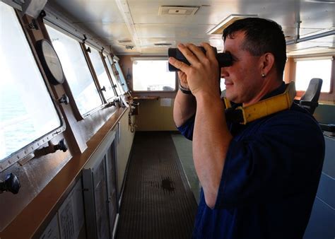 A photo of a seaman standing on the deck of a ship, with a futuristic-looking control panel in the background