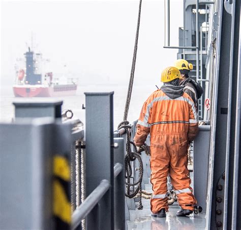 A photo of a seaman standing on the deck of a ship, with a harbor in the background